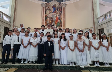 Después de recibir por primera vez el Cuerpo y la Sangre de Cristo, los niños posan felices en el presbiterio de la parroquia Don Rúa. 
