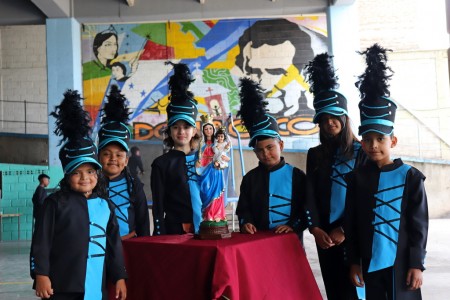Estudiantes de la banda escolar acompañan con orgullo y devoción la imagen de María Auxiliadora, durante el primer día de la novena celebrado en las canchas de la sede parroquial de Comayagüela.