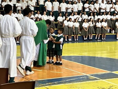 El padre José Manuel Solano, SDB, rector del Instituto Técnico Don Bosco, recibe con alegría las ofrendas presentadas por estudiantes de parvularia durante la solemne eucaristía de clausura del año lectivo 2024.