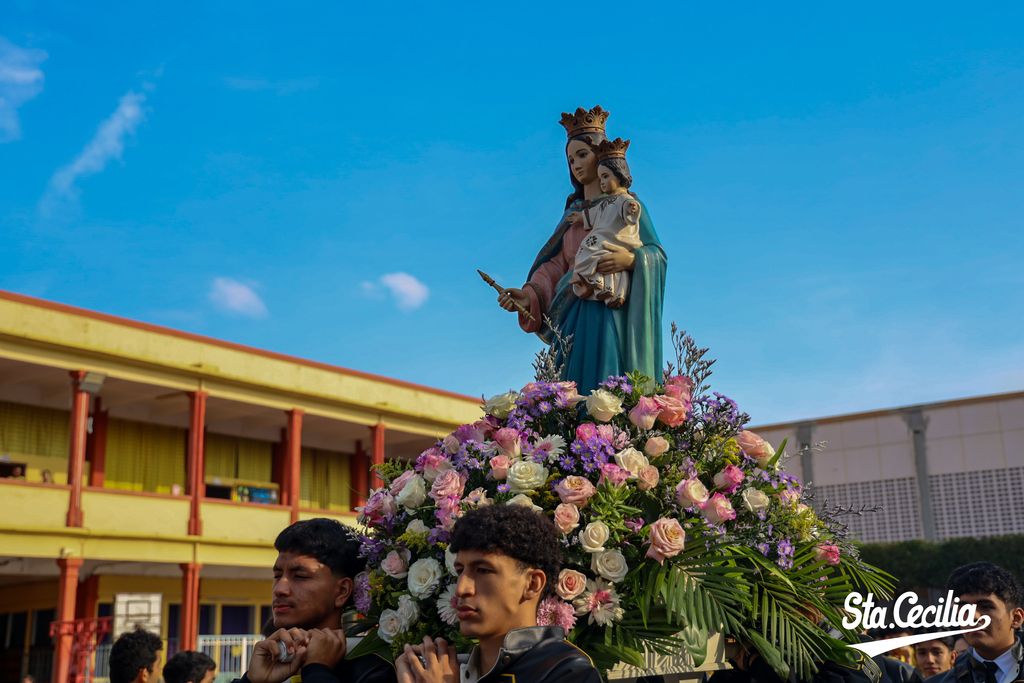 Jóvenes del Colegio Salesiano Santa Cecilia acompañan con fervor la imagen de María Auxiliadora durante la procesión por los patios del colegio, manifestando su amor y devoción a la Madre y Guía de la familia salesiana.